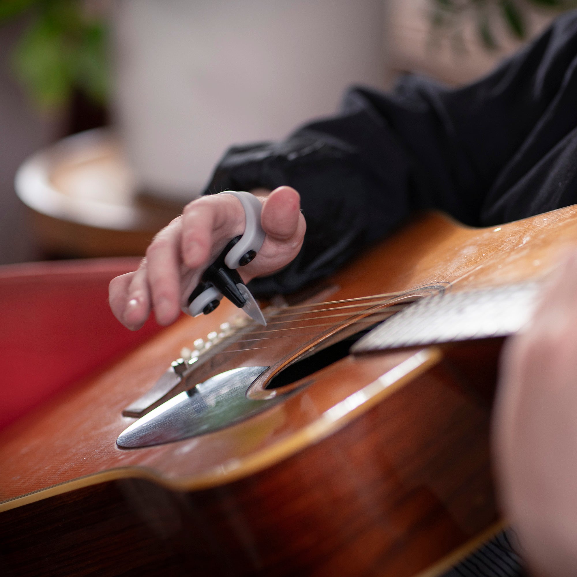 Person strumming an acoustic guitar with a Strumling pick holder on the hand.