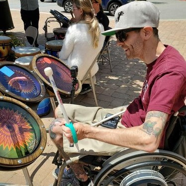 Man in a wheelchair playing a colorful drum with an aqua EazyHold srap on the drumstick.
