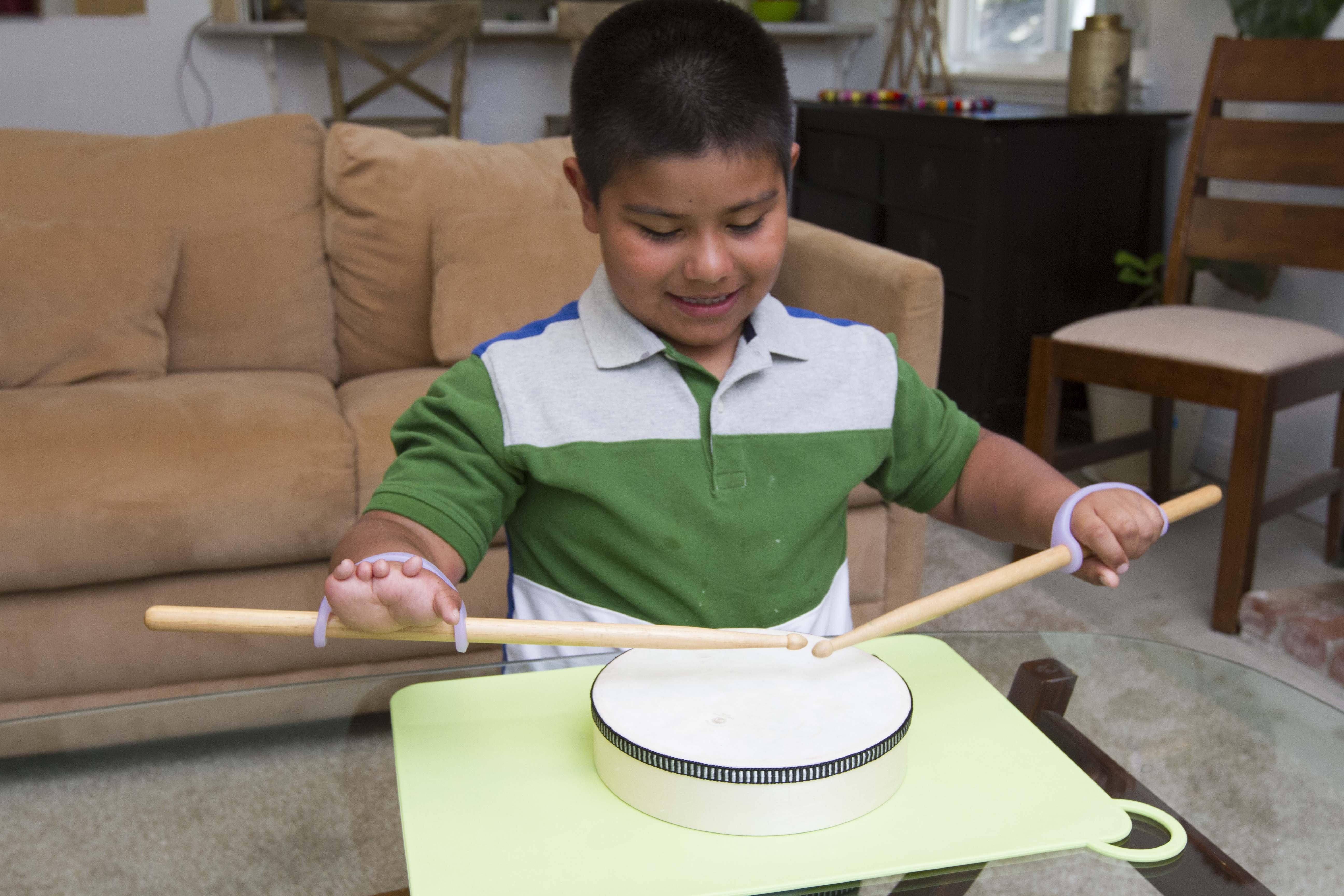 Boy plays the drums with lavender eazyholds on the drumsticks of hands with finger loss