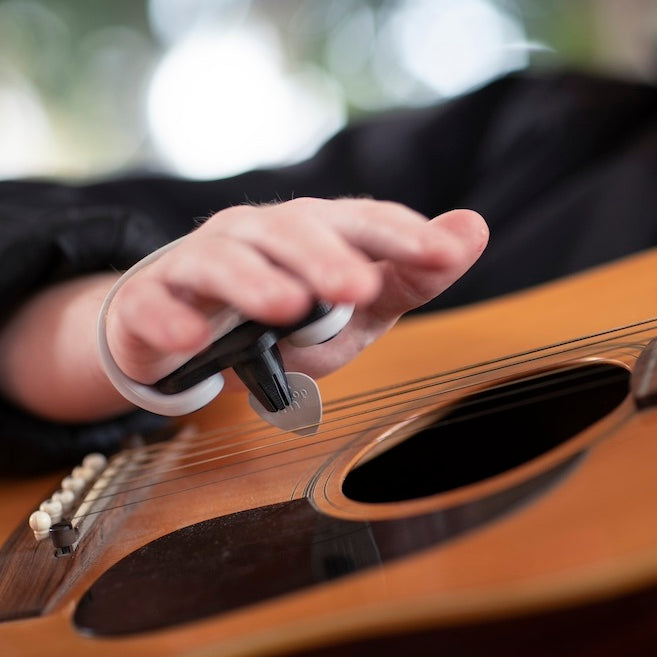 Person strumming an acoustic guitar with a Strumling pick holder on the hand.