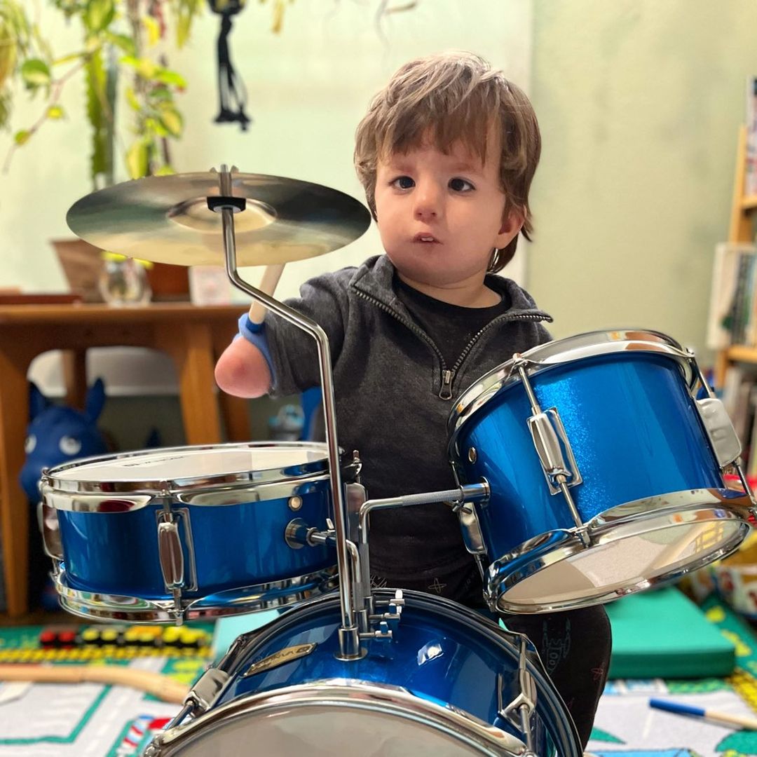 A child with no hands plays a blue drum set with a blue EazyHold on his drumstick.