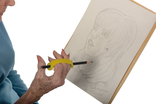 Woman draws with a yellow silicone assistive device to help her grasp the pencil.