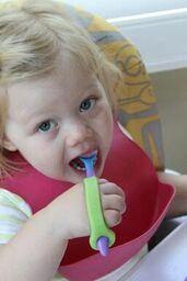 Child with special needs holding a spoon with a green adaptive eating aid