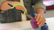 Child dipping an eazyhold adpted paintbrush into paint with a green silicone cuff.