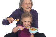 Mom and child with grip disabilities using pink eazyhold spoon adapters.