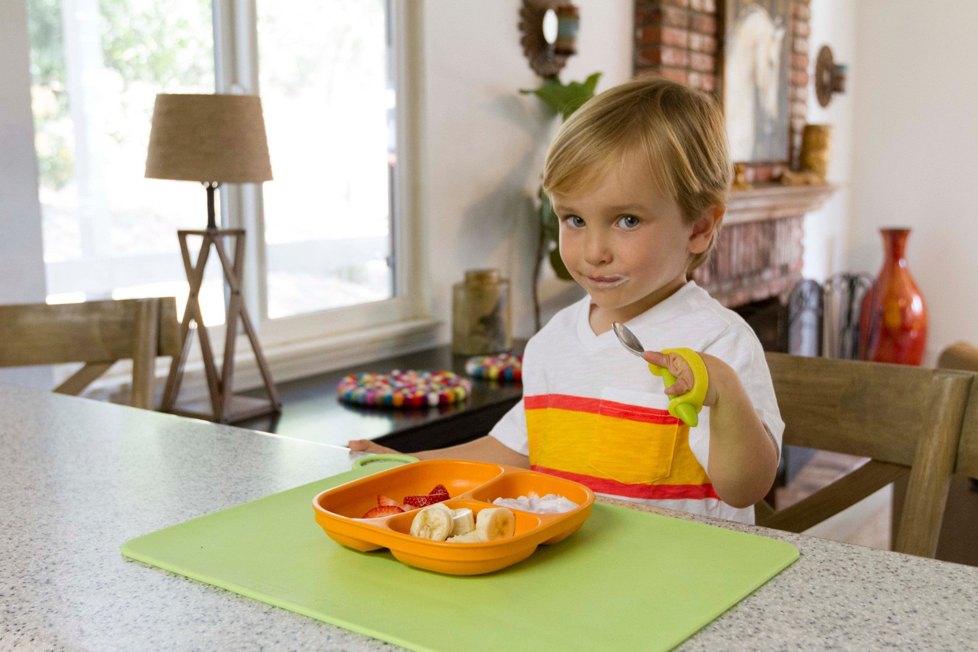 Young boy eating fruit and yogurt with a spoon held by a green EaZyHold cuff